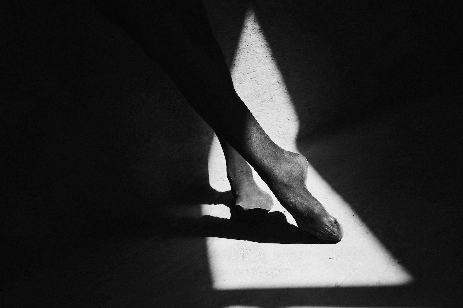 faceless ballerina resting feet on floor with shade.